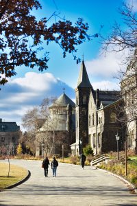 3 people walking along the King's College Circle path in front of University College.