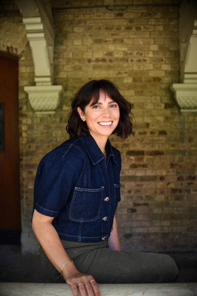 Haneen smiling and sitting in front of a brick exterior.