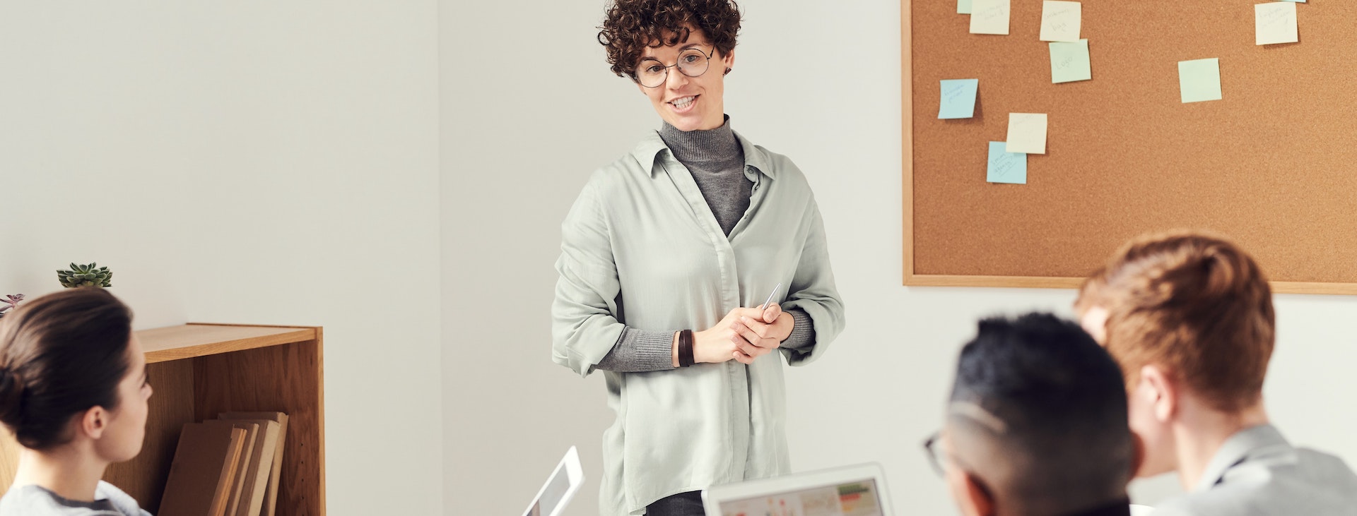 Person presenting in front of corkboard to group of three