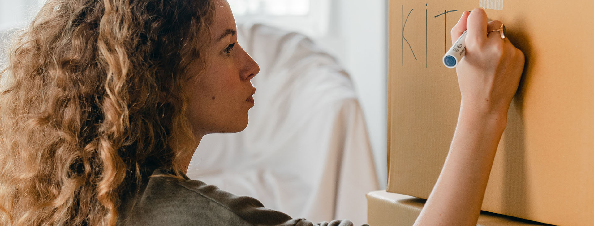 Young woman writing KITCHEN on a cardboard box